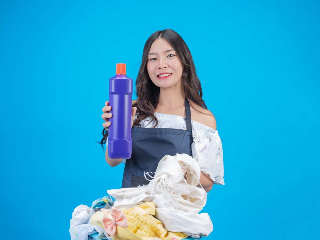 A beautiful woman holding a cloth and liquid detergent prepared for washing on a blue background.
